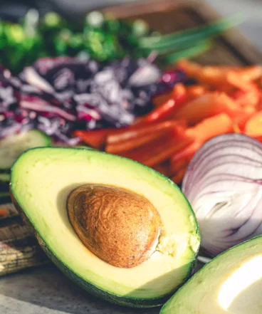 avocado-halves-kitchen-table-with-chopped-fresh-vegetables.webp